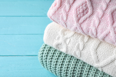 Stack of folded warm sweaters on turquoise wooden background, closeup