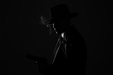 Photo of Old fashioned detective with gun smoking cigarette on dark background, black and white effect