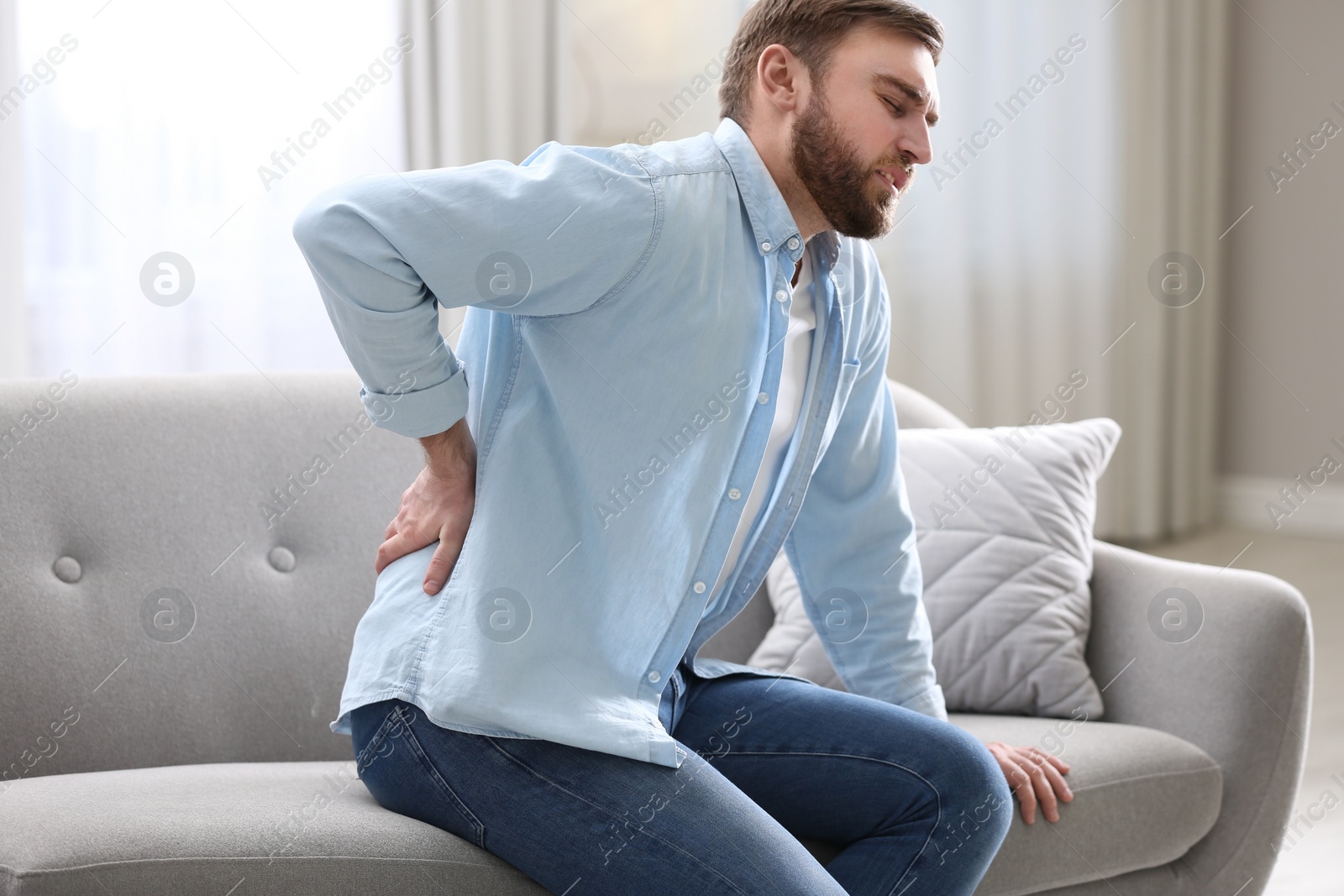 Photo of Man suffering from back pain at home. Bad posture problem