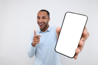 Photo of Young man showing smartphone in hand and pointing at it on white background