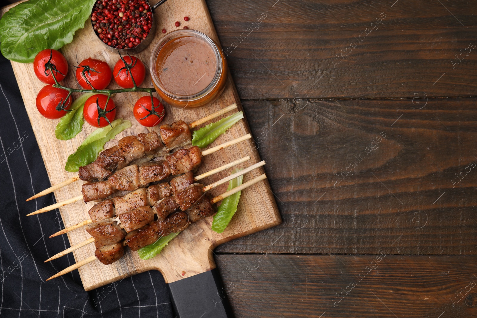 Photo of Tasty cooked marinated meat served with sauce and tomatoes on wooden table, flat lay. Space for text