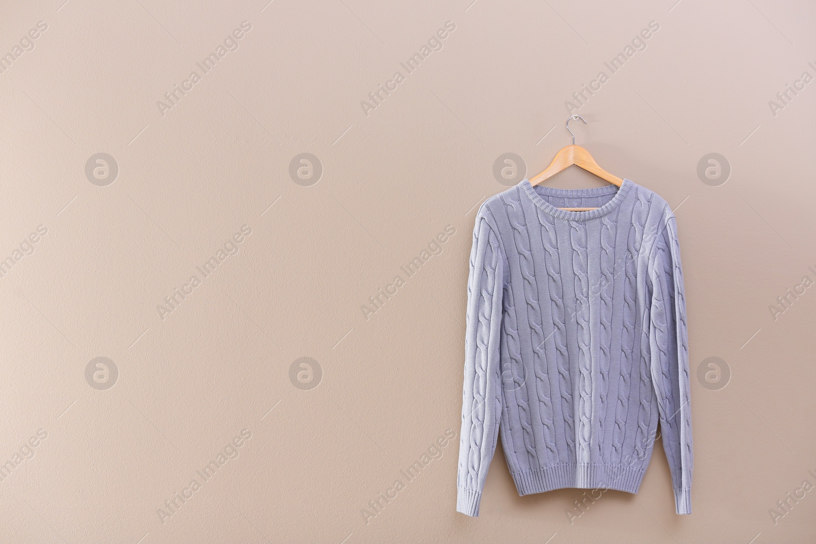 Photo of Hanger with stylish sweater on beige wall. Space for text