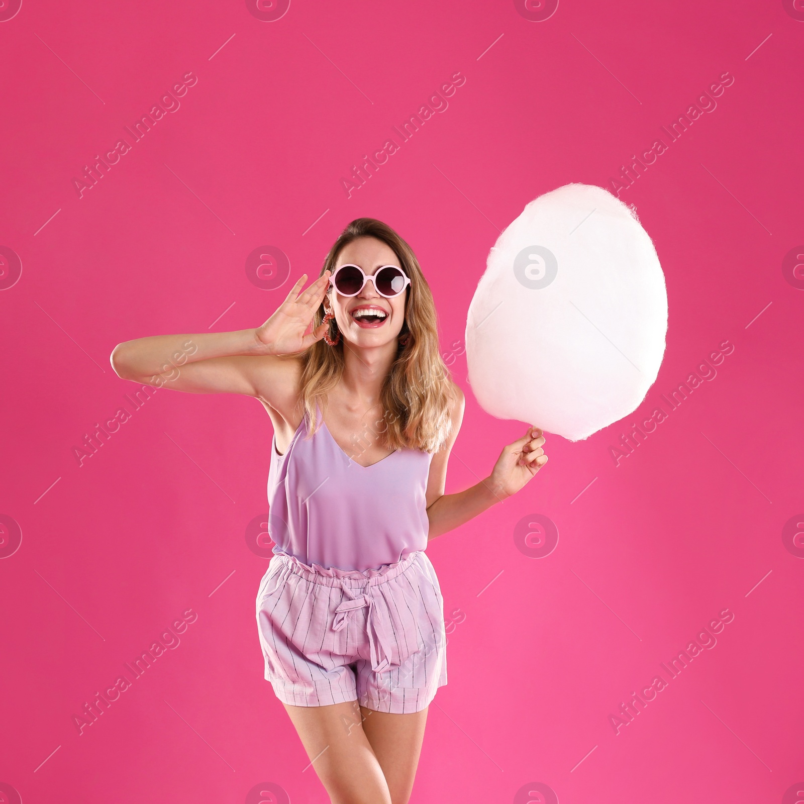 Photo of Happy young woman with cotton candy on pink background