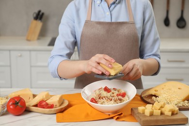 Woman grating cheese onto delicious pasta at white marble table in kitchen, closeup