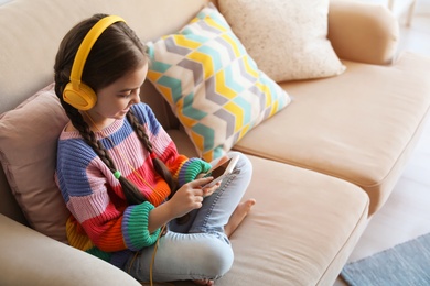 Photo of Cute child with headphones and mobile phone on sofa indoors. Space for text