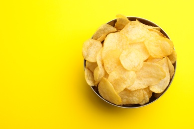 Photo of Delicious crispy potato chips in bowl on color background, top view with space for text