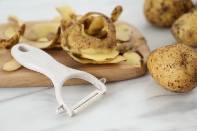 Photo of Potato, peels and peeler on white marble table, closeup