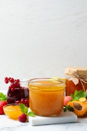Photo of Jars with different jams and fresh fruits on white marble table