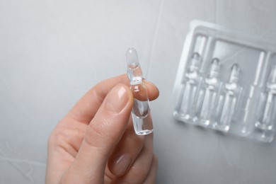 Photo of Woman holding pharmaceutical ampoule with medication at light grey table, top view