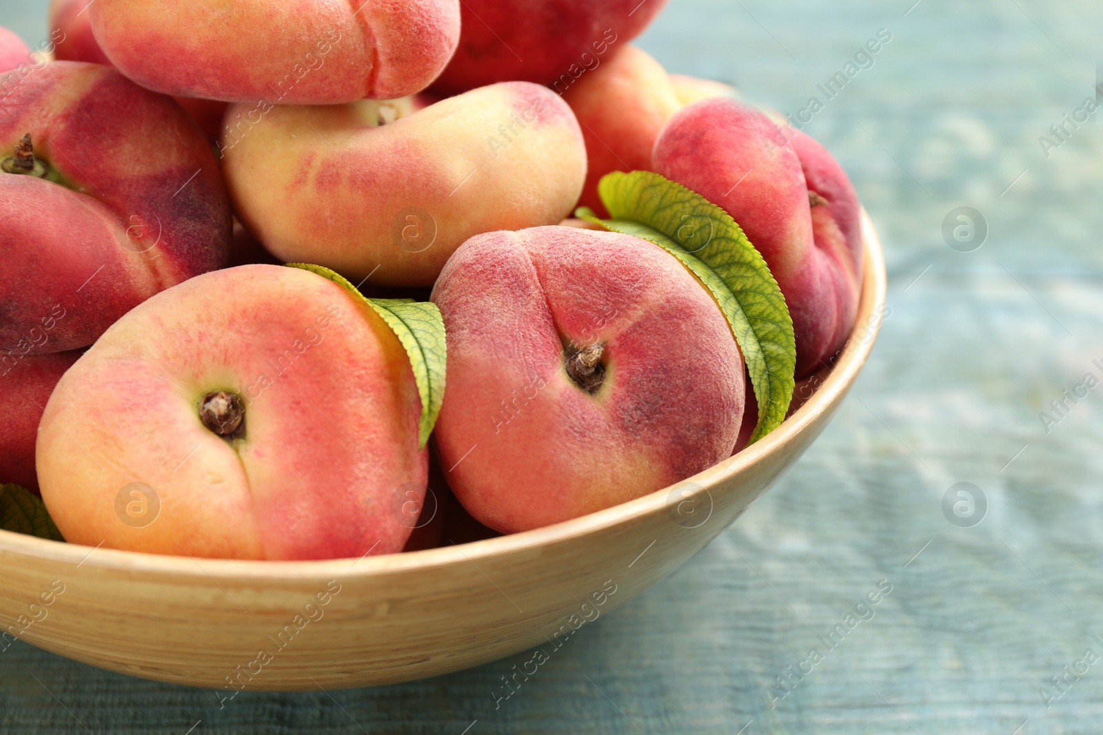 Photo of Fresh ripe donut peaches in bowl on light blue wooden table, closeup