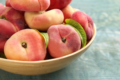 Photo of Fresh ripe donut peaches in bowl on light blue wooden table, closeup