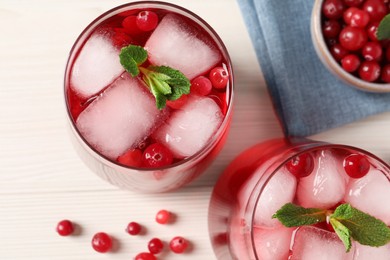 Tasty cranberry juice with ice cubes in glasses and fresh berries on white wooden table, flat lay