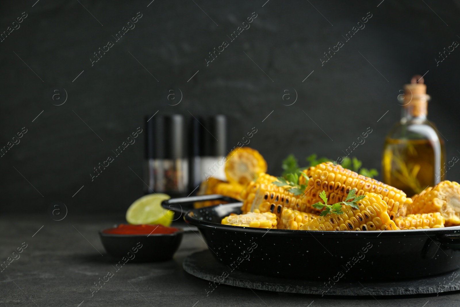 Photo of Pan with tasty grilled corn on dark grey table. Space for text