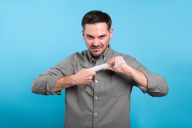 Emotional man with bubble wrap on light blue background