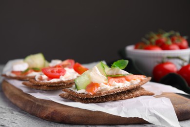 Photo of Tasty rye crispbreads with salmon, cream cheese and cucumber on wooden board, closeup