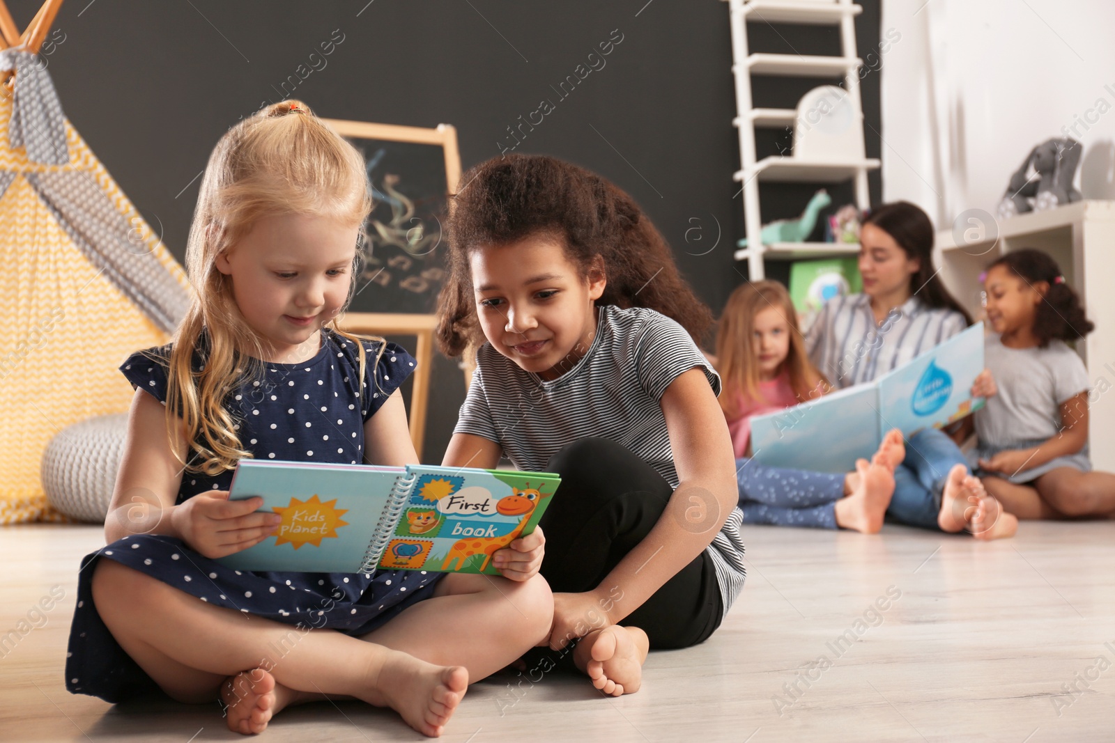 Photo of Cute little children reading book on floor in kindergarten, space for text. Indoor activity