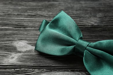 Photo of Stylish green satin bow tie on black wooden background, closeup