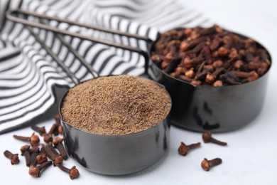 Photo of Aromatic clove powder and dried buds in scoops on white table, closeup
