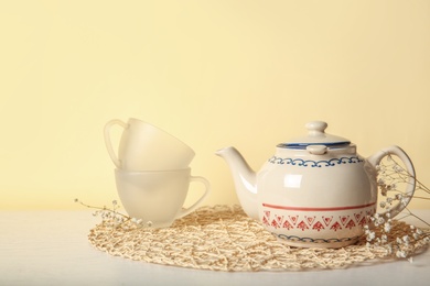 Teapot and cups on table against color background