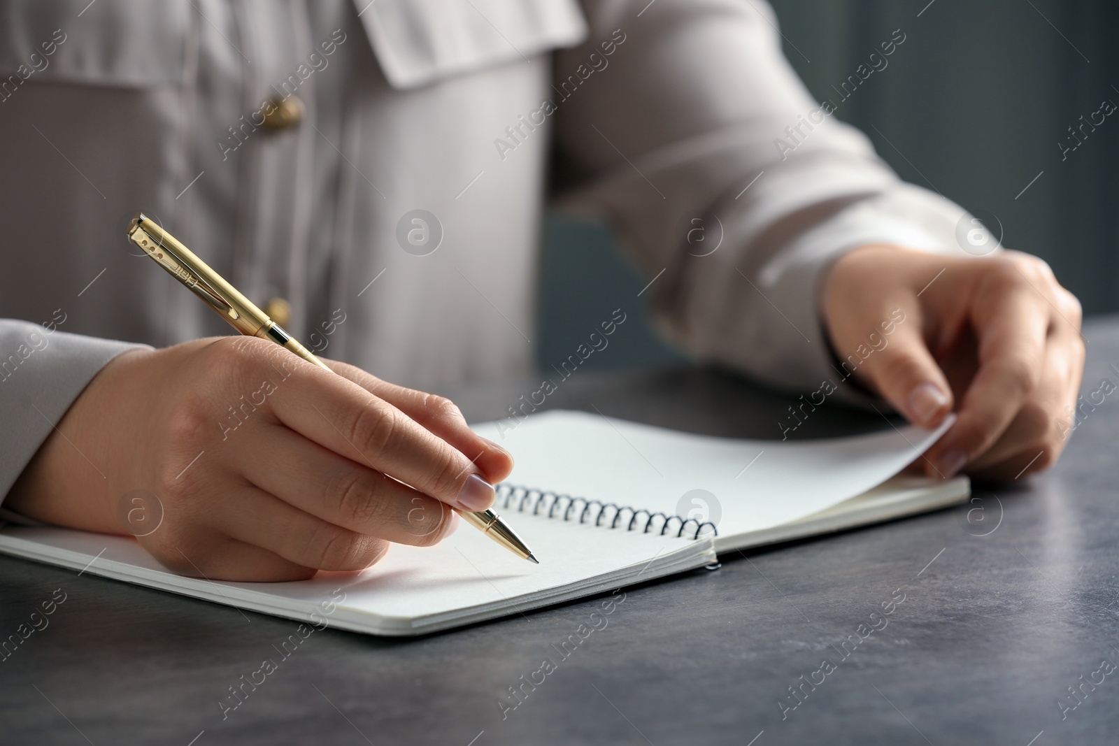 Photo of Woman writing in notebook with pen at grey table, closeup