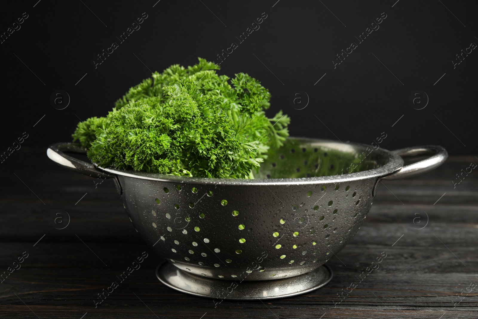 Photo of Colander with fresh green parsley on dark wooden table against black background