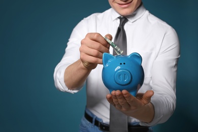 Businessman putting money into piggy bank on color background, closeup. Space for text