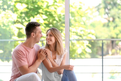 Photo of Happy young couple sitting near window at home