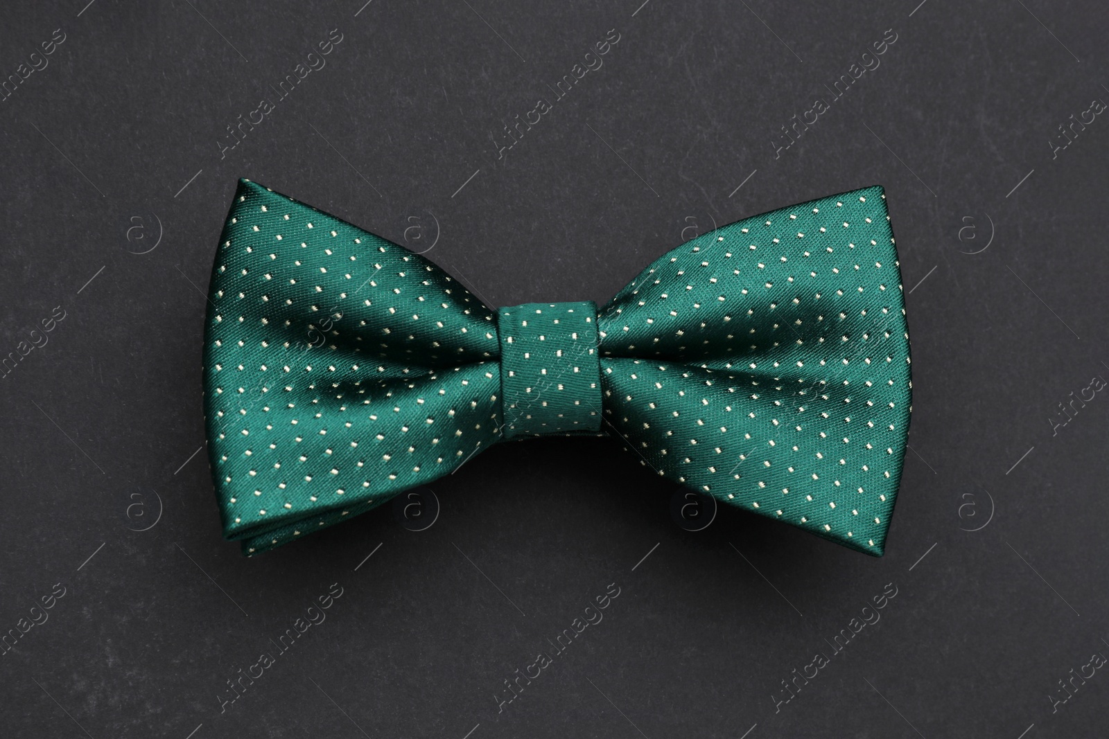 Photo of Stylish green bow tie with polka dot pattern on black background, top view
