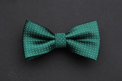 Stylish green bow tie with polka dot pattern on black background, top view