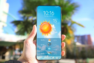 Image of Man using weather forecast app on smartphone outdoors on sunny day, closeup. Data, sun and other illustrations on screen