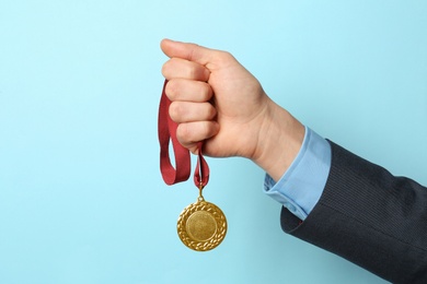 Photo of Man holding golden medal on color background, closeup. Space for text