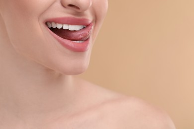 Young woman licking her teeth on beige background, closeup