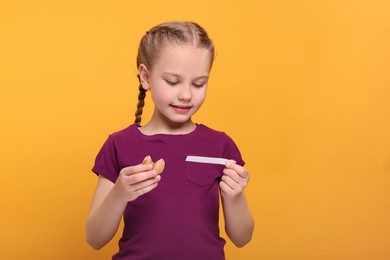 Photo of Cute girl holding tasty fortune cookie and reading prediction on orange background