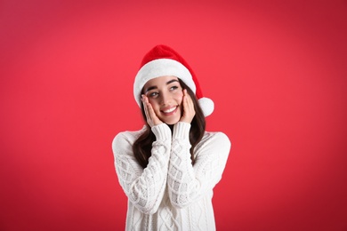 Beautiful woman wearing Santa Claus hat on red background