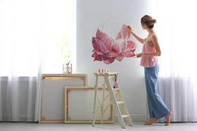 Decorator painting flower on white wall in room. Interior design