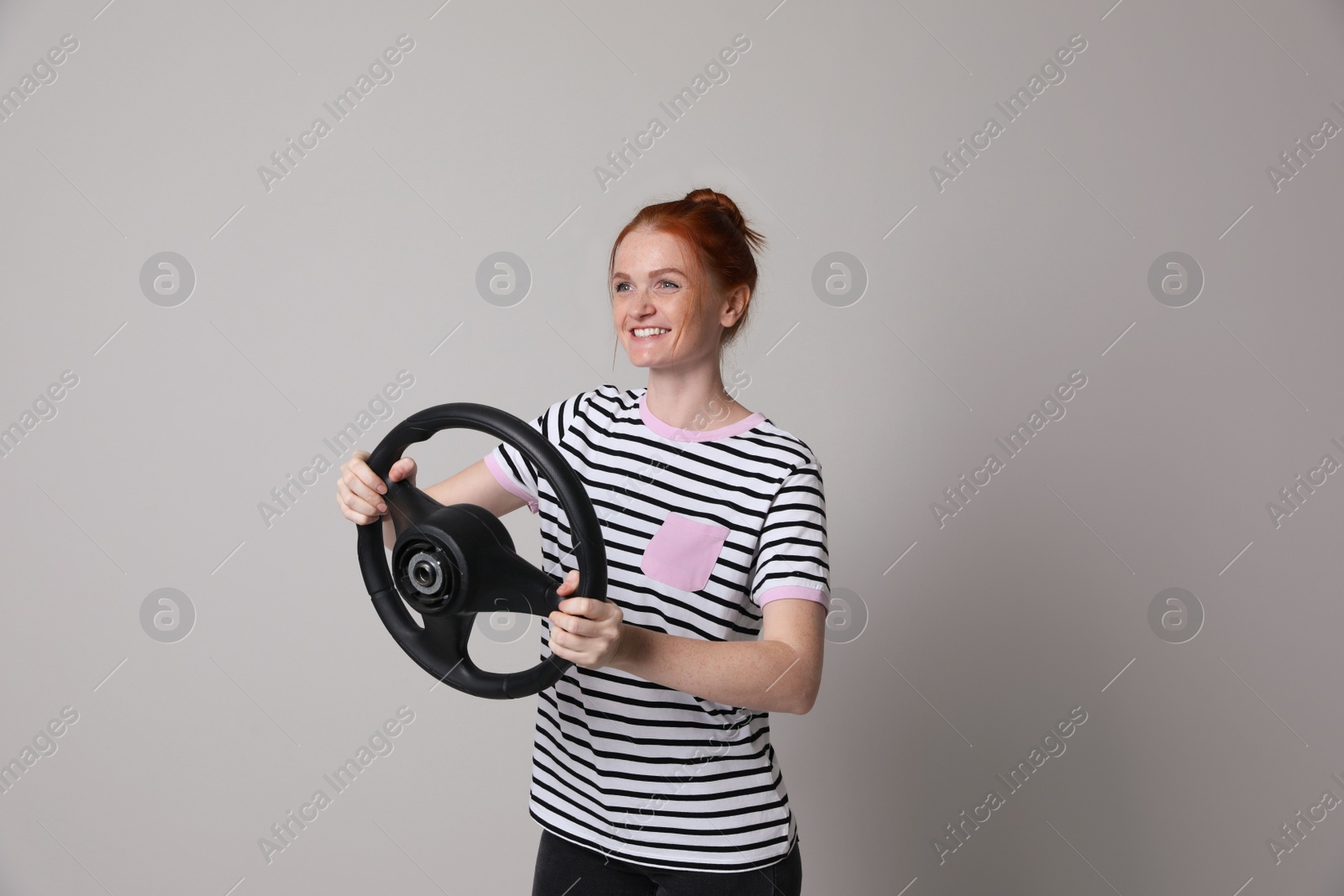Photo of Happy young woman with steering wheel on grey background