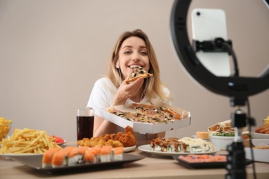 Photo of Food blogger recording eating show on smartphone camera against beige background. Mukbang vlog