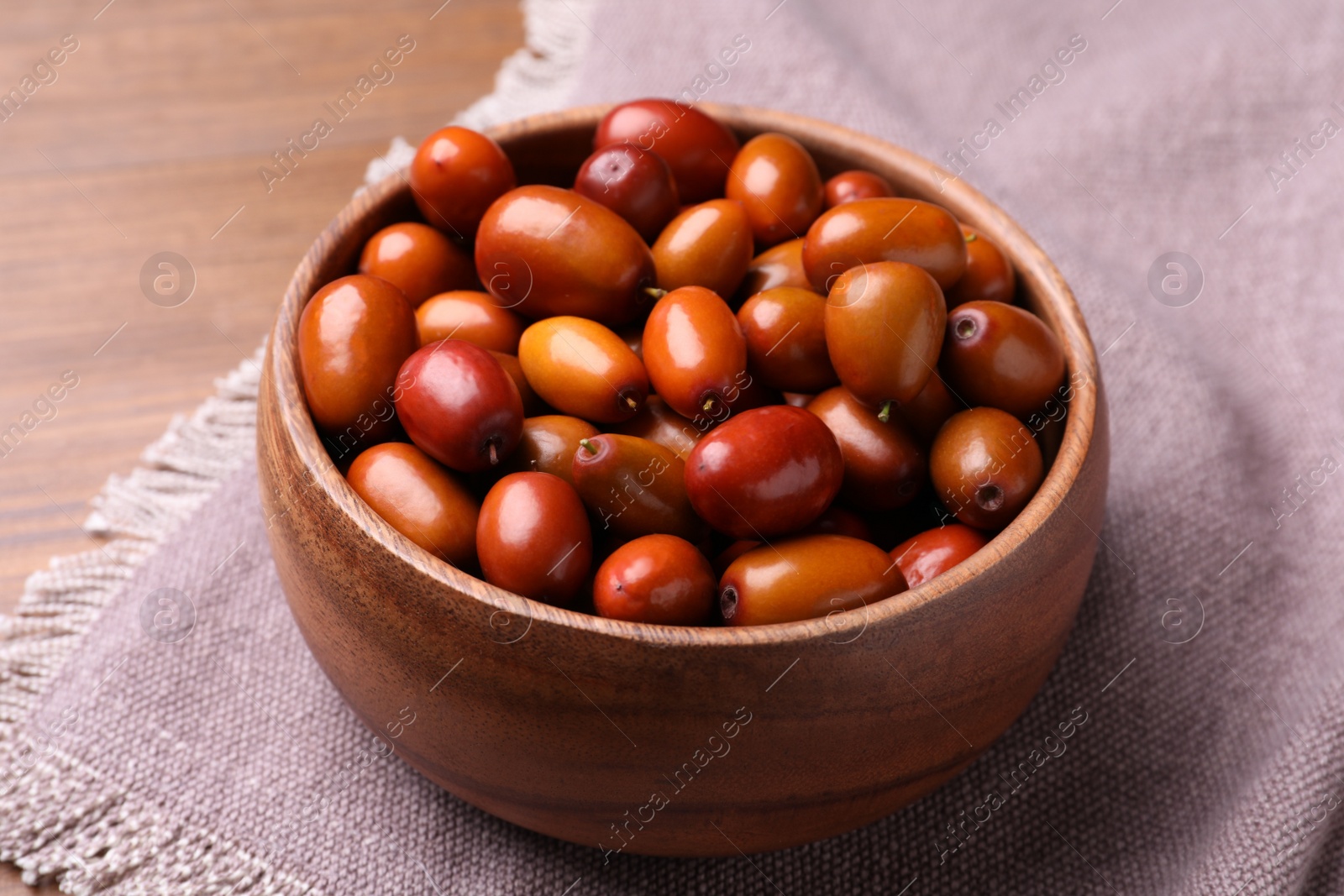 Photo of Fresh Ziziphus jujuba fruits in wooden bowl on table, closeup