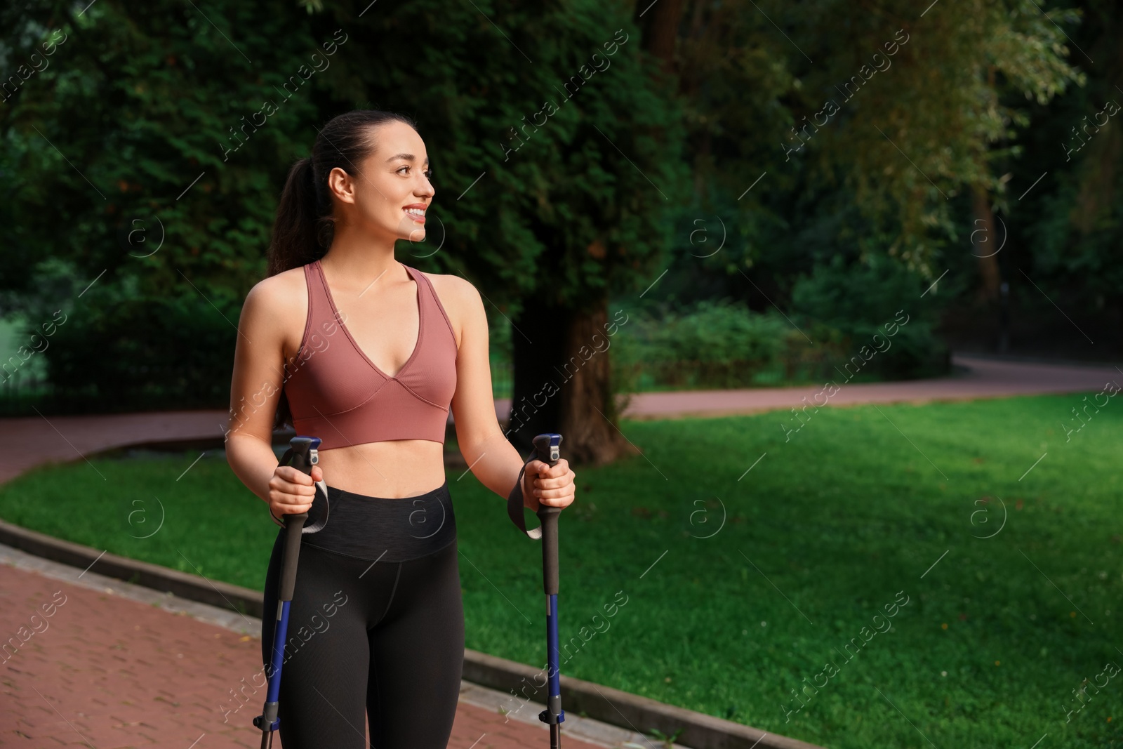 Photo of Young woman practicing Nordic walking with poles outdoors. Space for text