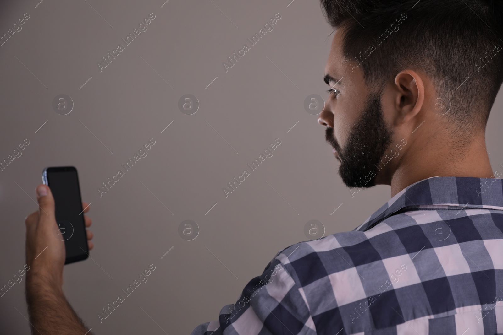 Photo of Young man unlocking smartphone with facial scanner on beige background. Biometric verification