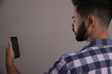 Young man unlocking smartphone with facial scanner on beige background. Biometric verification