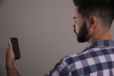 Photo of Young man unlocking smartphone with facial scanner on beige background. Biometric verification