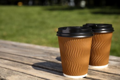 Photo of Takeaway cardboard coffee cups with plastic lids on wooden bench outdoors, space for text