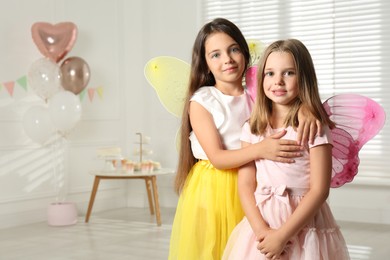 Photo of Cute little girls wearing fairy costumes in decorated room. Space for text