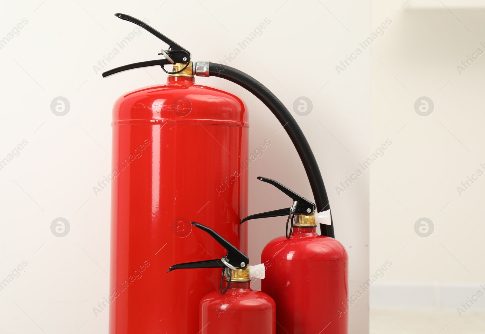 Photo of Three fire extinguishers near light wall indoors