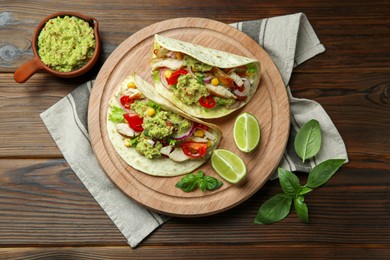 Photo of Delicious tacos with guacamole, meat and vegetables served with lime on wooden table, flat lay
