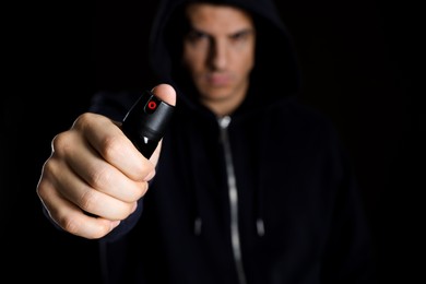 Photo of Man using pepper spray against black background, focus on hand. Space for text