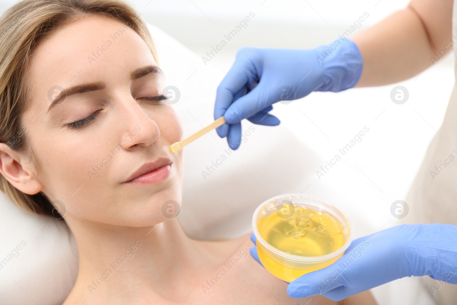 Photo of Beautiful woman getting wax epilation of face in salon