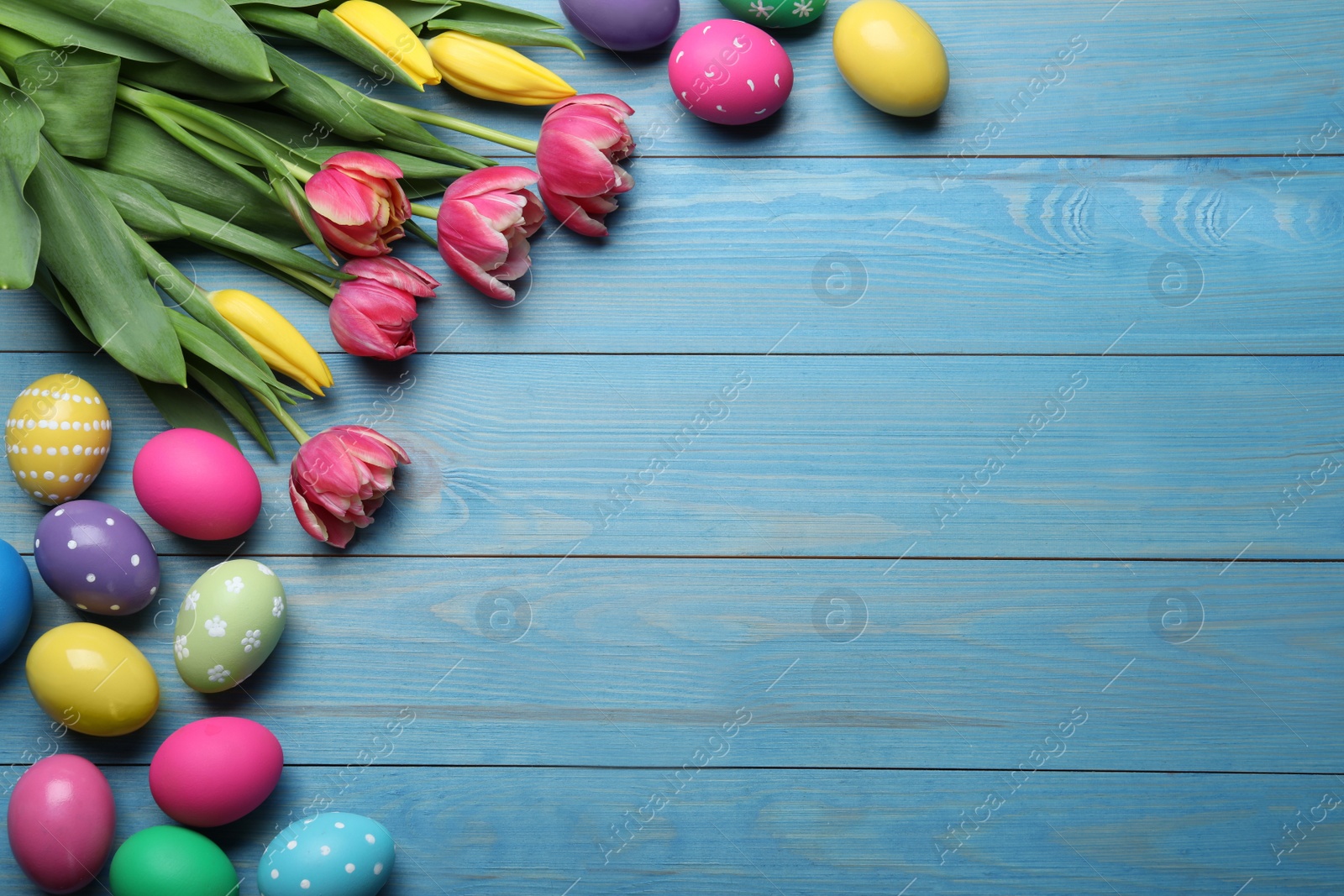 Photo of Colorful eggs and tulips on blue wooden background, flat lay with space for text. Happy Easter