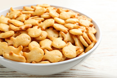 Delicious goldfish crackers in bowl on white wooden table, closeup